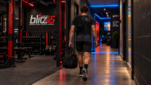 Blitz45 member walking from the strength floor toward the glowing blue Recovery Room doorway.