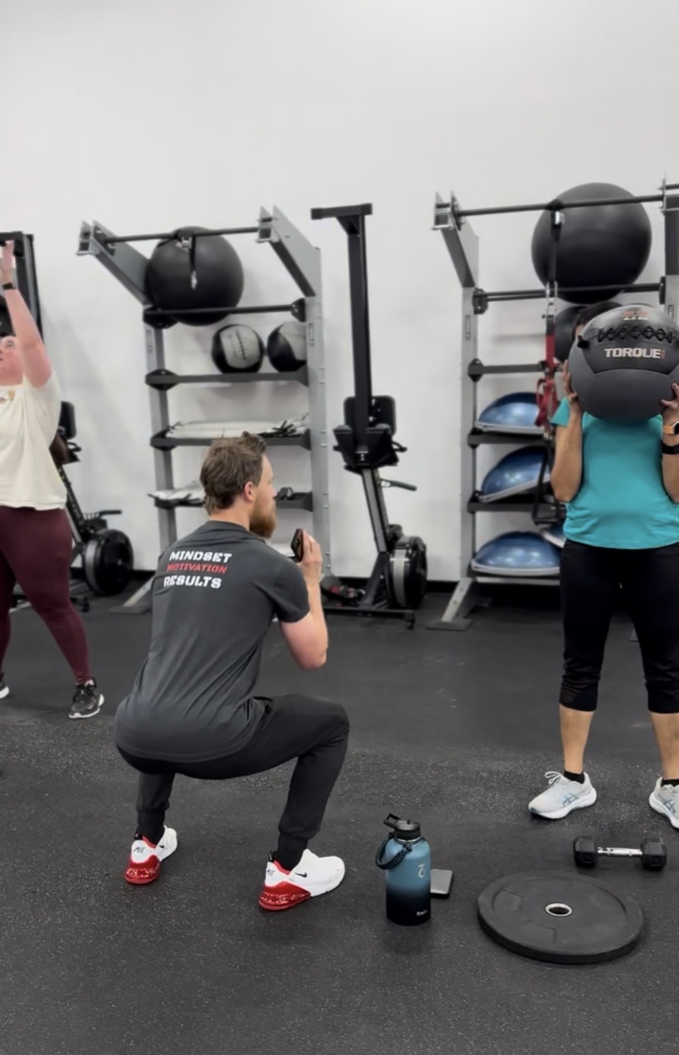 Blitz45 coach guiding a small group through a squat with medicine balls
